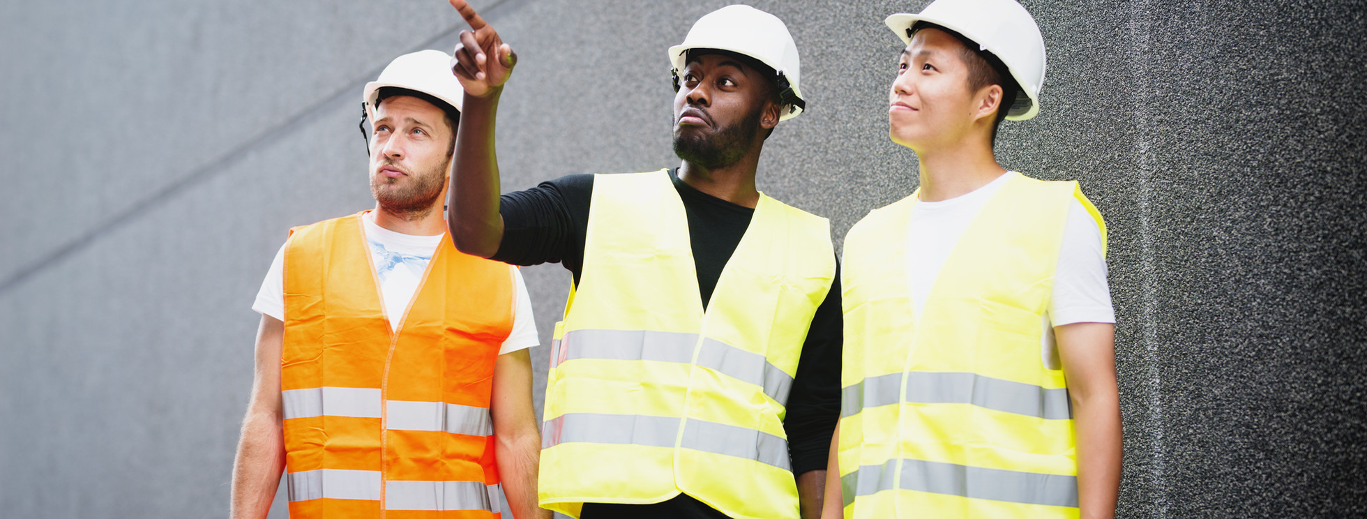 Three construction professionals wearing hard hats and high-visibility vests